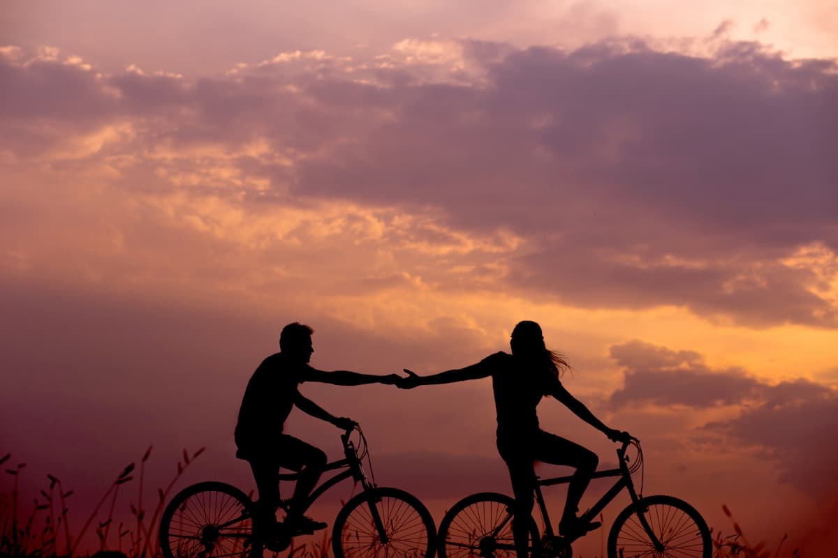Paar auf Fahrrädern hält sich an den Händen vor Sonnenuntergang